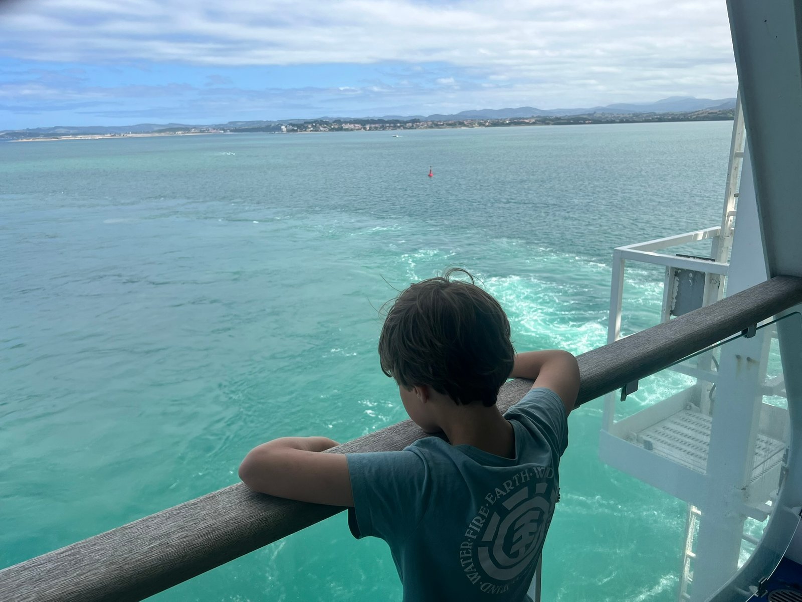 Niño en la barandilla del ferry mirando aparecer la costa